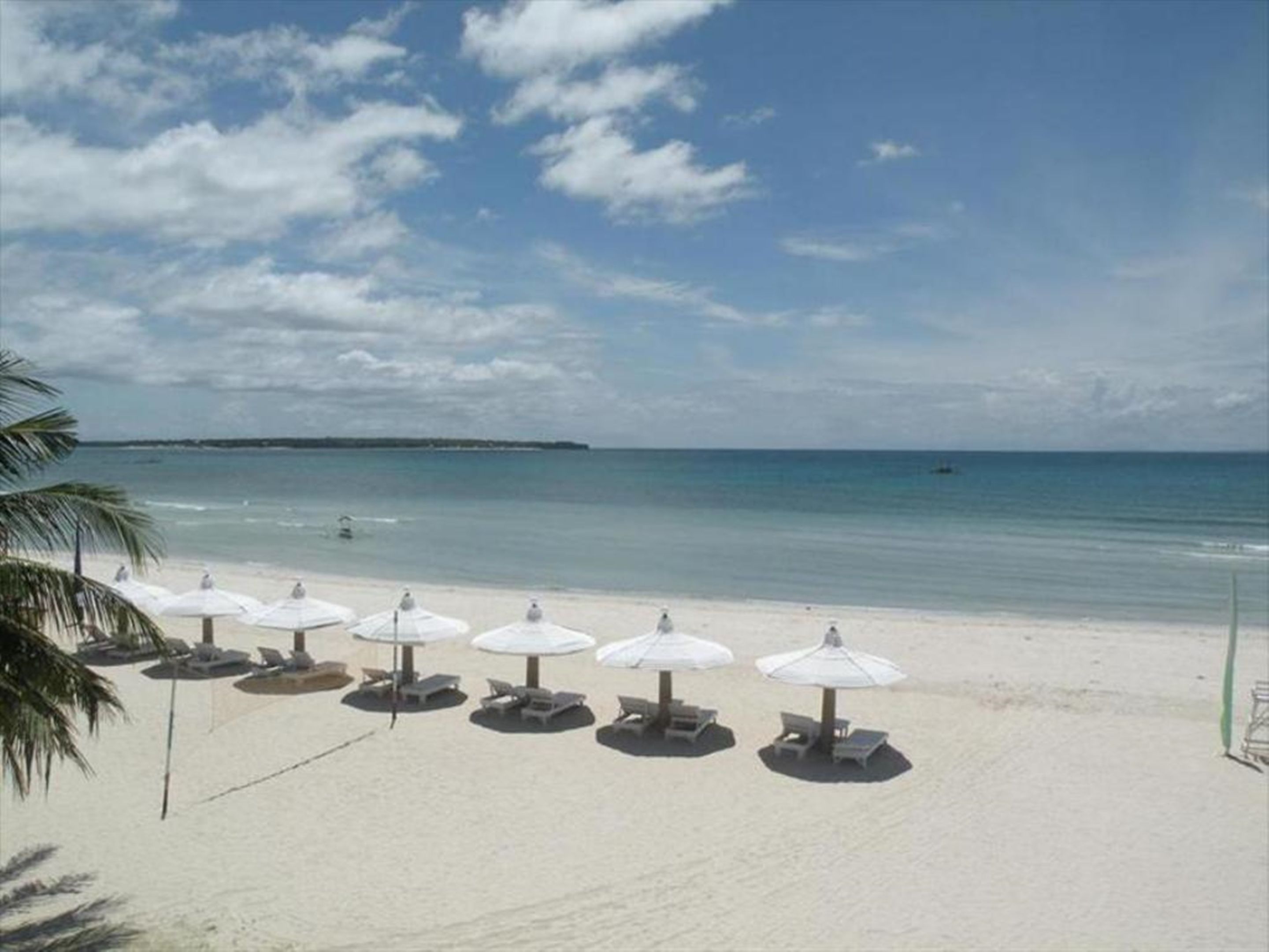 Une plage avec des parasols blancs et des chaises longues, un ciel dégagé et une mer calme.