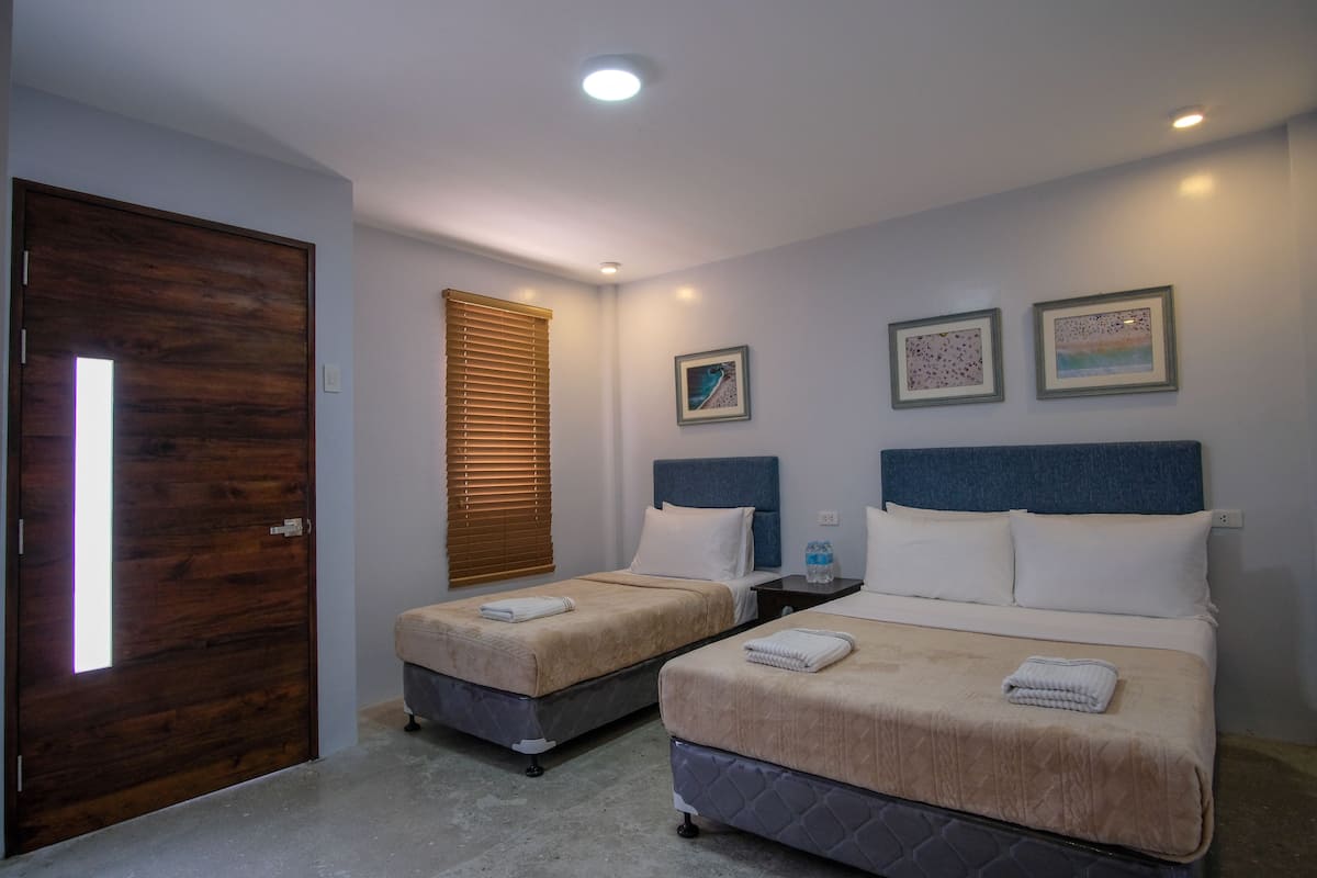 A hotel room with two beds, a wooden door, a window with blinds, and three framed pictures on the wall.