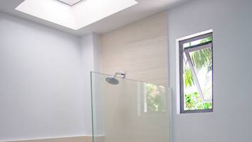 A modern bathroom with a glass-enclosed shower, a toilet, and a small window with a view of greenery.