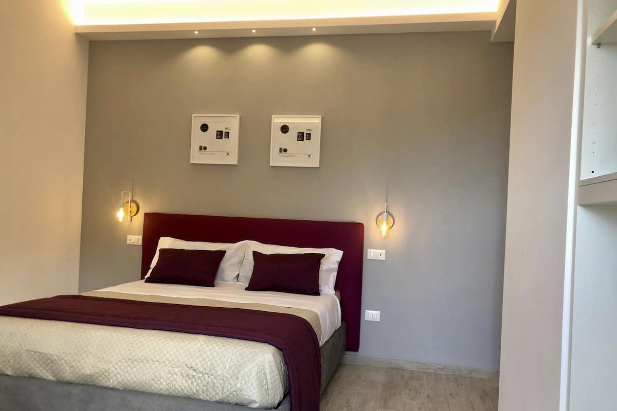 A hotel room with a bed, two wall-mounted light fixtures, and a ceiling light.