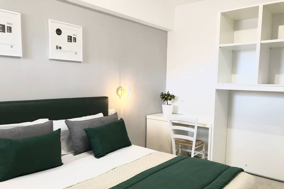 A modern bedroom with a bed, bedside tables, a wall-mounted light, and a potted plant.