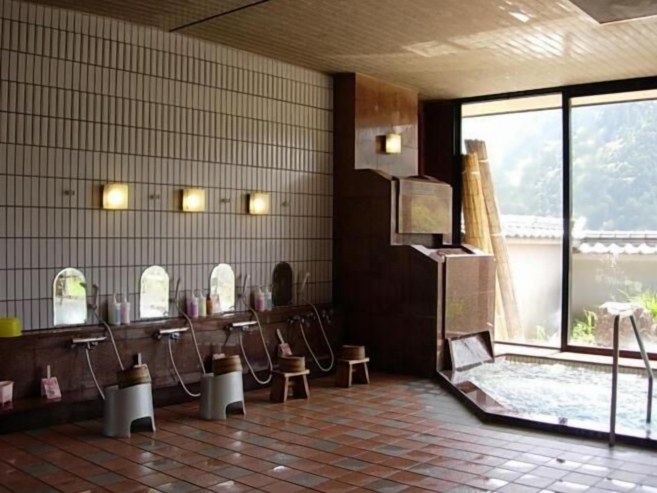 A traditional Japanese onsen with tiled walls, wooden benches, and a view of the outdoors.