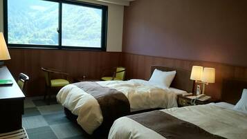 A hotel room with two beds, a desk, a chair, and a window with a mountain view.