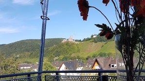 Ein Tisch mit einer Flasche und einem Glas auf einem Balkon mit Blick auf eine hügelige Landschaft, Häuser und ein Schloss.