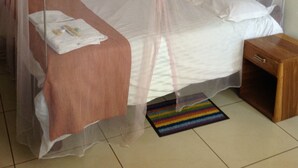 A single bed with a mosquito net, a bedside table, and a small wooden nightstand. - Standard Way Lodge (Livingstone)