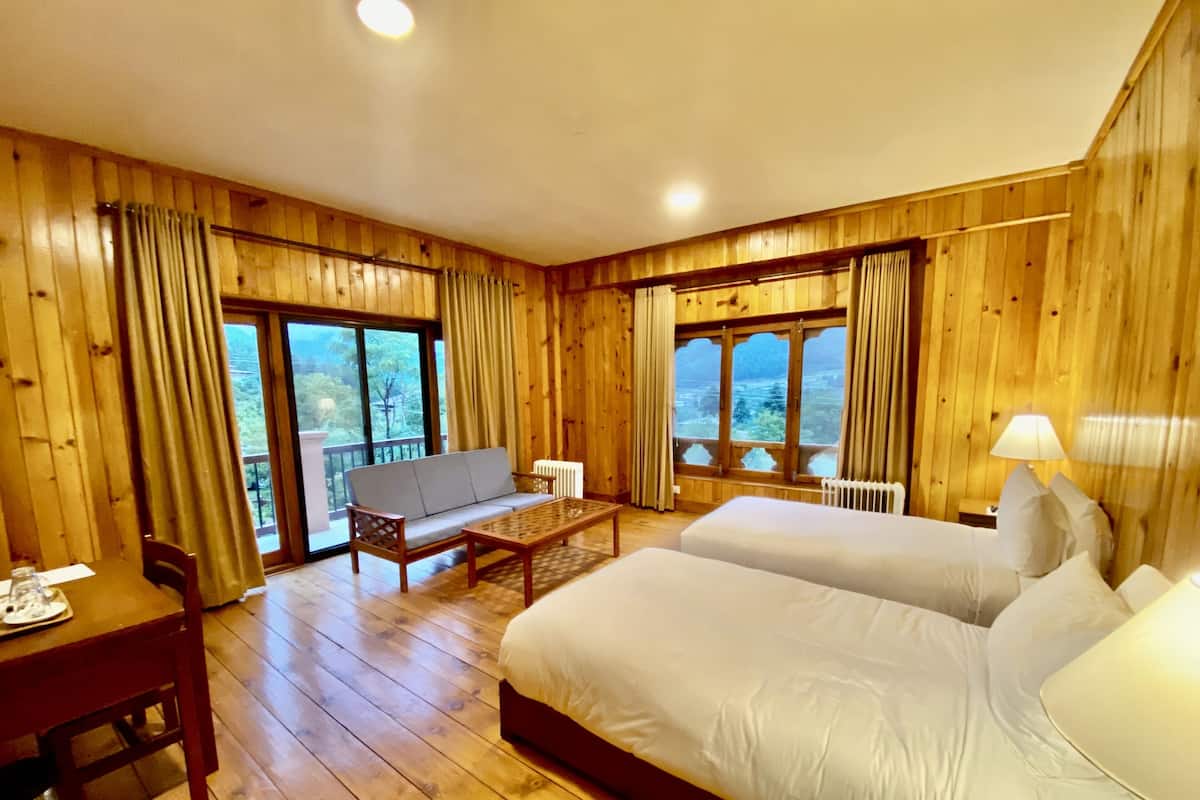 A wooden room with two beds, a sofa, a table, and large windows offering a view of the outdoors.