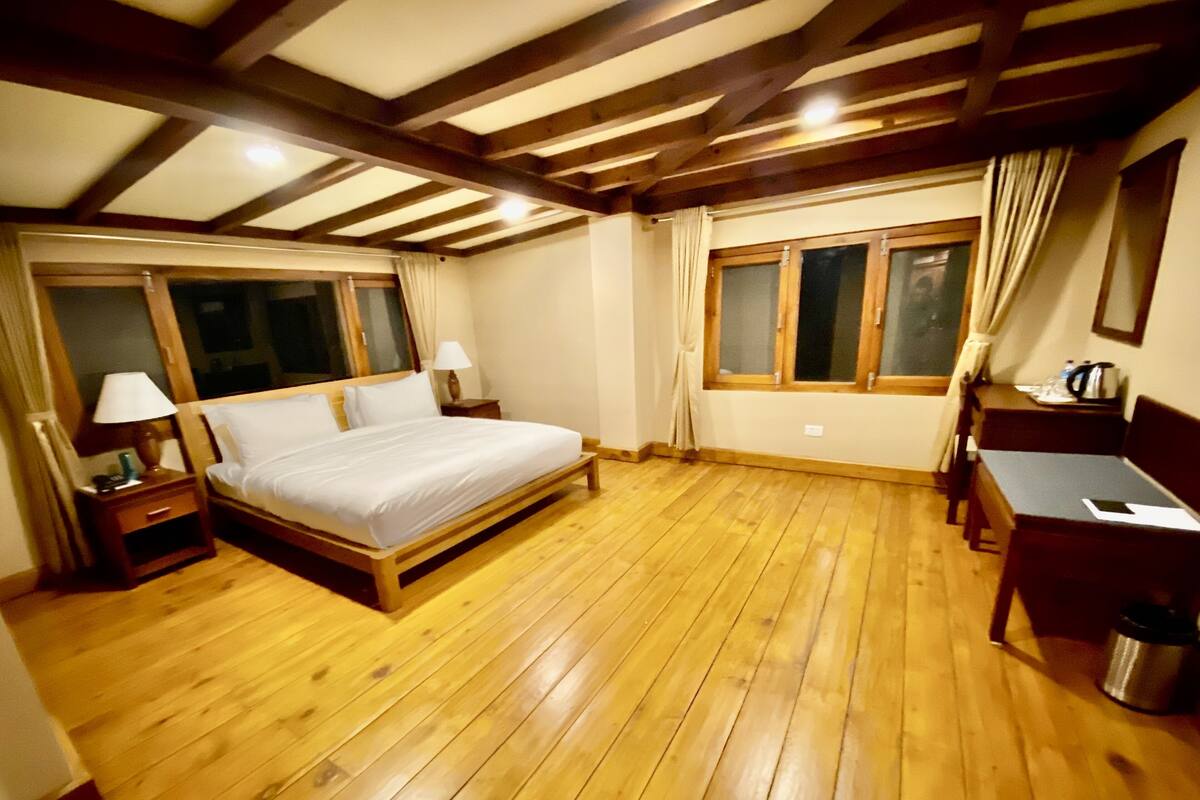 A bedroom with a wooden bed, two bedside tables, a desk, and a window with curtains.