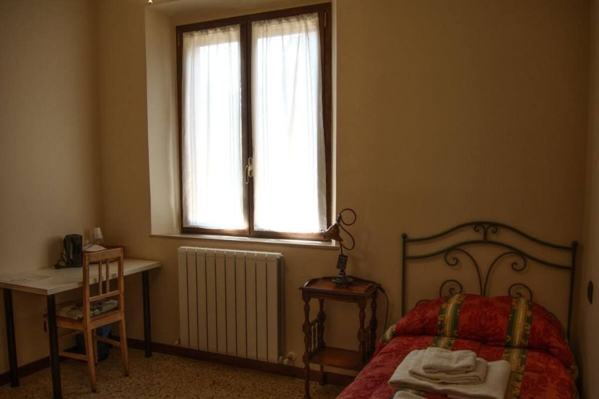 A bedroom with a bed, a desk, a chair, a radiator, and a window.