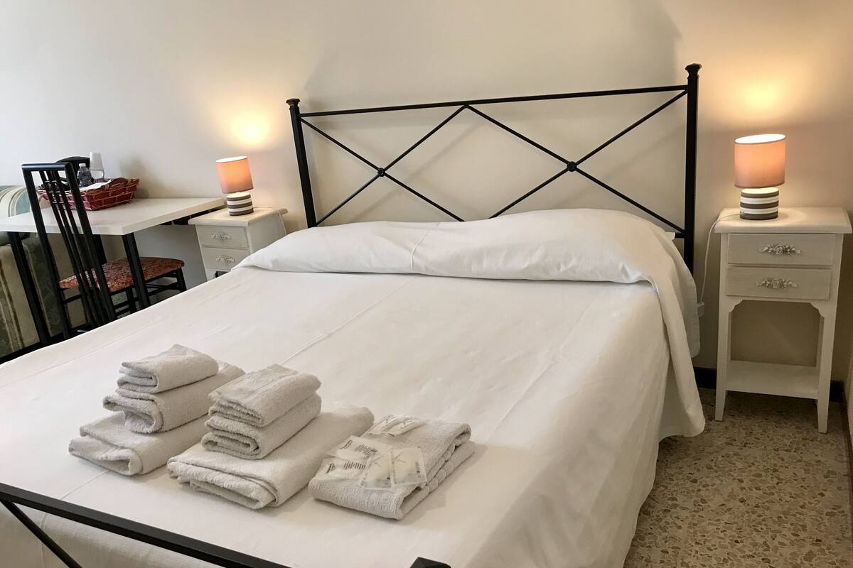 A neatly made bed with white linens and folded towels, a black metal headboard, and bedside tables with lamps.