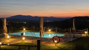 Una piscina con lettini e ombrelloni, circondata da una recinzione e con vista sulle montagne.