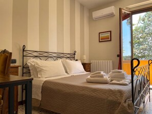 Un letto rifatto con lenzuola bianche, un comodino con una lampada e una finestra con vista sugli alberi.