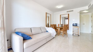 Ein Wohnzimmer mit einer Couch, einem Esstisch mit Stühlen, einer Mikrowelle und einem kleinen Schrank.