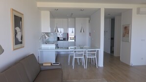 A modern living room with a glass dining table, white chairs, and a beige sofa. - A beautiful one bedroom apartment - right on the waterfront in the Ria Formosa. (Fuseta)