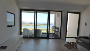 A spacious living area with a large sliding glass door leading to a balcony with a view of the sea. - A beautiful one bedroom apartment - right on the waterfront in the Ria Formosa. (Fuseta)