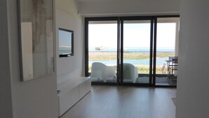 A spacious room with a large sliding glass door leading to a balcony with a view of the sea. - A beautiful one bedroom apartment - right on the waterfront in the Ria Formosa. (Fuseta)