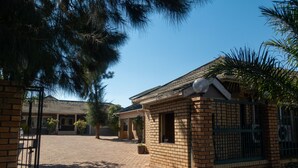 A brick house with a paved driveway and a gated entrance. - Trench Town Lodge (Livingstone)