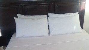 A neatly made bed with a wooden headboard and white bedding. - Trench Town Lodge (Livingstone)