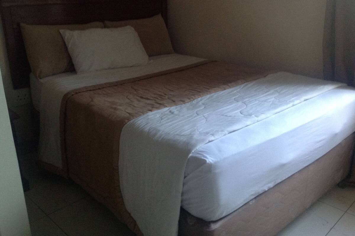 A bed with a wooden headboard, white bedding, and a brown blanket.