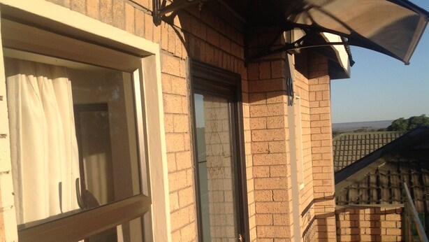 A balcony with a glass door, a window with curtains, and a brick wall. - Trench Town Lodge (Livingstone)