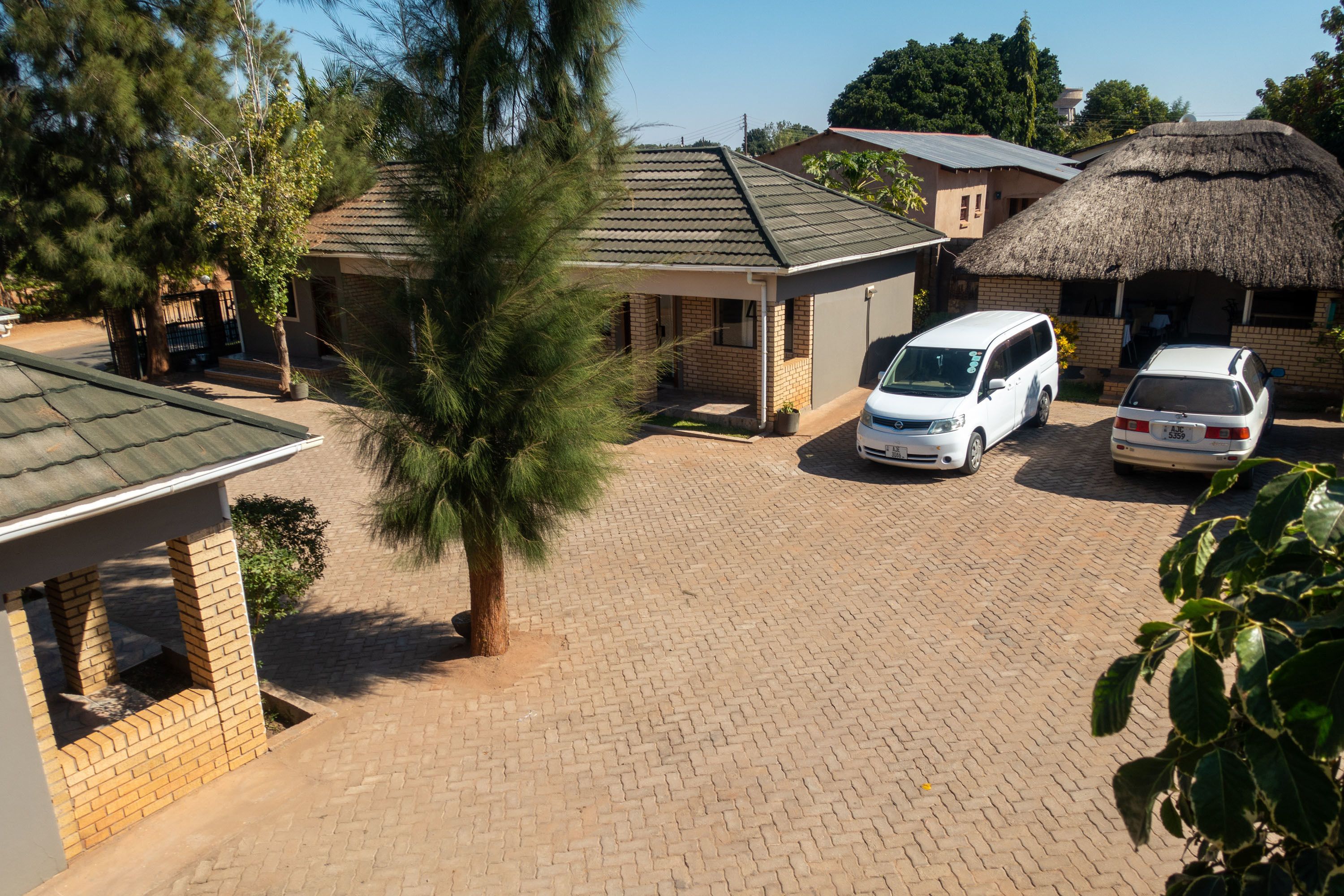 A residential area with a paved driveway, two parked white vans, and a thatched-roof building.