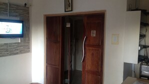 A room with a wooden door, a television mounted on the wall, and a small table with a document on it. - Trench Town Lodge (Livingstone)