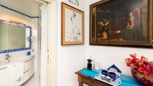 A bathroom with a white sink, blue-tiled mirror, framed artwork, and a vase of flowers. - Marino Suite Sorrento (Sorrento)