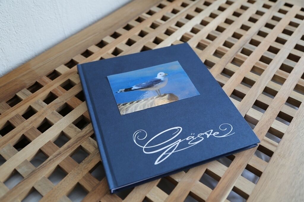 A book with a seagull photo and the word "Gäste" on a wooden lattice table.