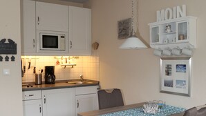 A compact kitchen with white cabinets, a microwave, and a coffee maker. There is a dining table with chairs and a hanging light fixture. - Welcome to our "Möwennest" apartment in a prime location! WIRELESS INTERNET ACCESS (Sankt Peter-Ording)