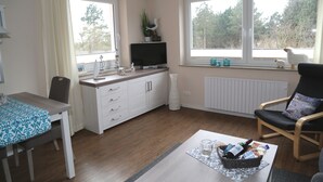 A modern living room with a dining area, a television, and a window with a view of trees. - Welcome to our "Möwennest" apartment in a prime location! WIRELESS INTERNET ACCESS (Sankt Peter-Ording)