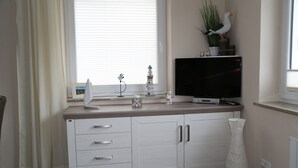 A modern living room with a flat-screen TV, white cabinetry, a potted plant, and a decorative vase. - Welcome to our "Möwennest" apartment in a prime location! WIRELESS INTERNET ACCESS (Sankt Peter-Ording)