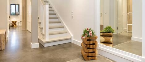 Un intérieur moderne avec un escalier, un jardinier en bois orné de fleurs et un grand miroir qui reflète une salle de bain.