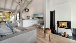 A modern living room with a fireplace, a sofa, and a dining area with a view. - AS1C - Old barn (AS) at c a l l s e n - appartements (Ummanz)