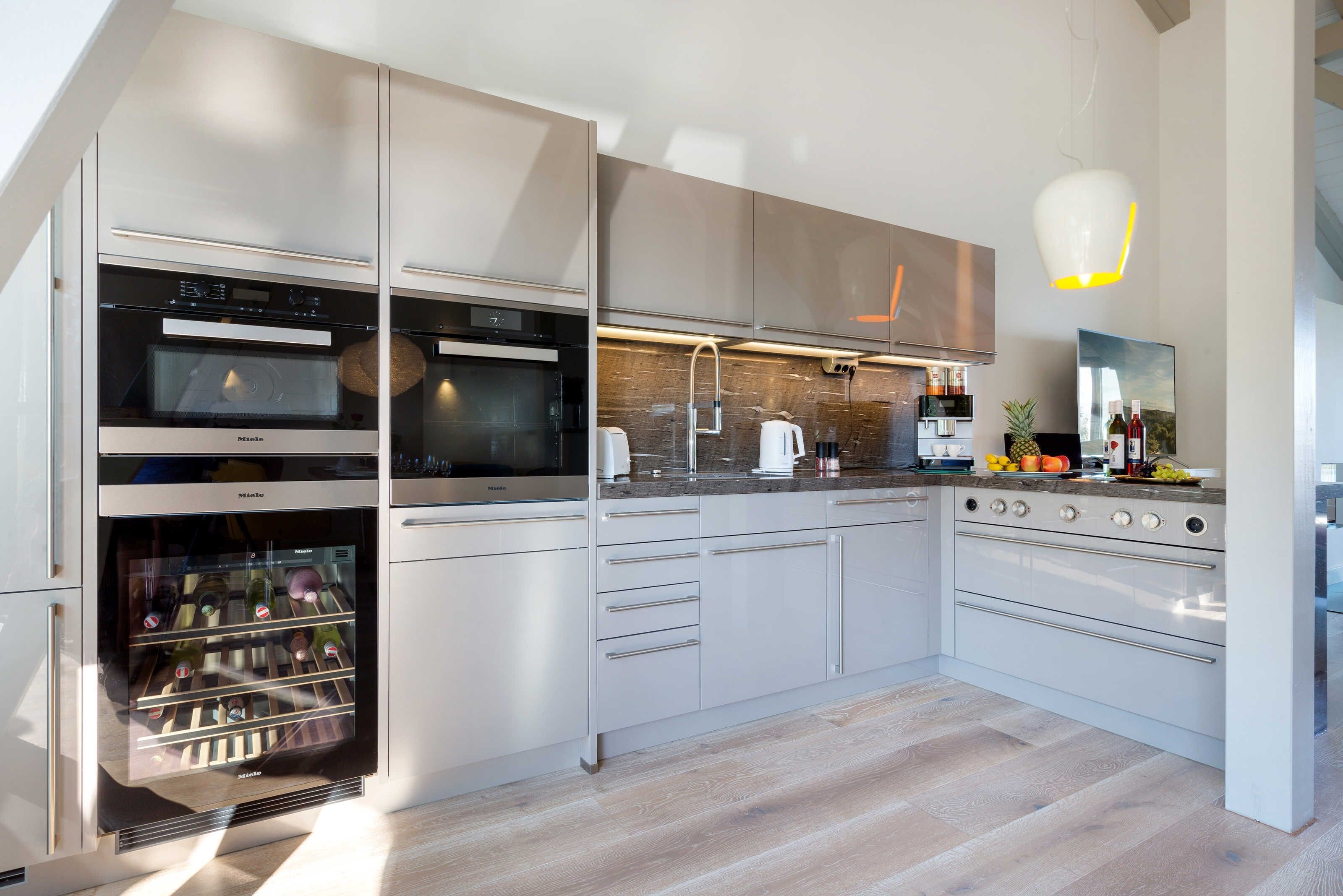 A modern kitchen with built-in appliances, a wooden floor, and a hanging light fixture.