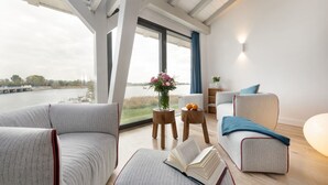 A modern living room with a large window, a sofa, a coffee table, and a bookshelf. - AS1C - Old barn (AS) at c a l l s e n - appartements (Ummanz)