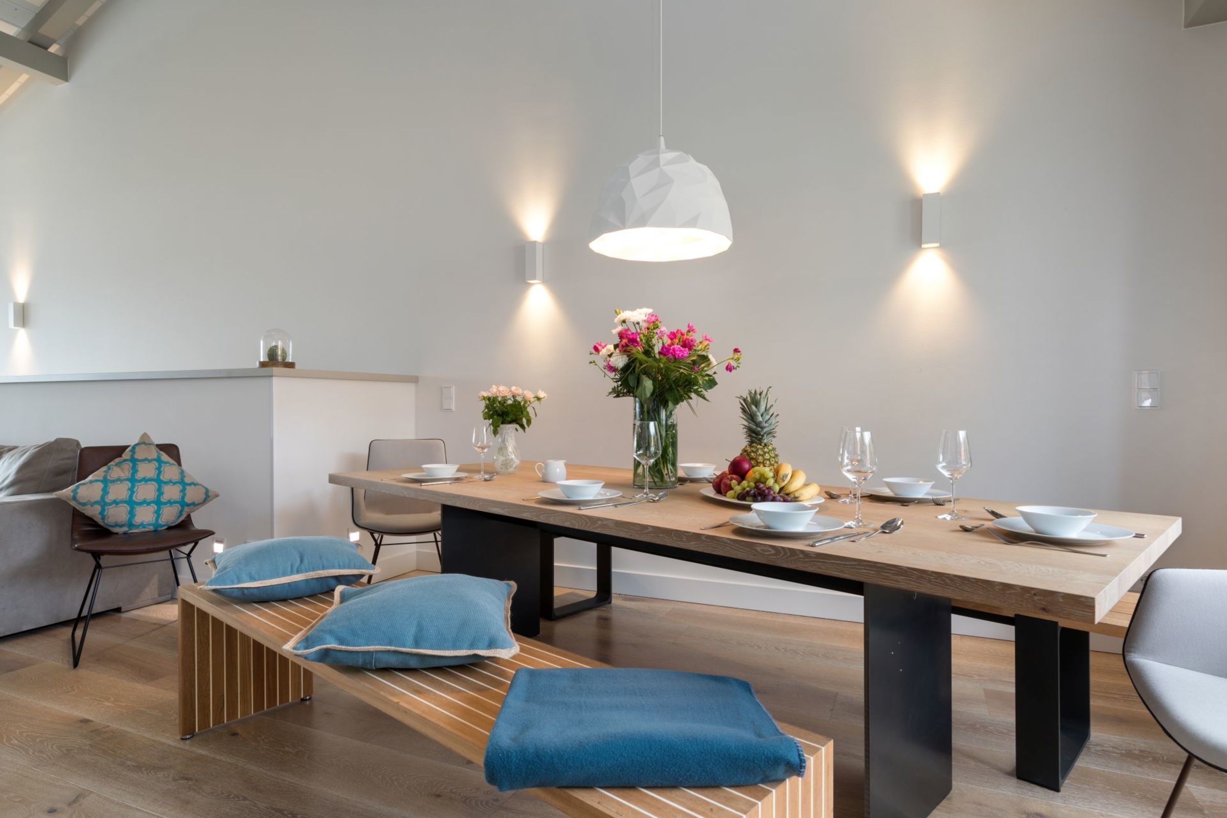 Uma área de jantar moderna com mesa de madeira, bancos e iluminação pendente.