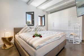 Un dormitorio moderno con una cama grande, una mesita de noche de madera, un armario blanco y un televisor montado en la pared.