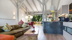 A modern living room with a wooden coffee table, a sofa with patterned cushions, and a kitchen area with a dark countertop and a hanging light fixture. - AS1C - Old barn (AS) at c a l l s e n - appartements (Ummanz)