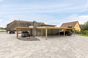 Un espacio exterior cubierto con un porche, un edificio de techo de paja y un camino de entrada pavimentado.