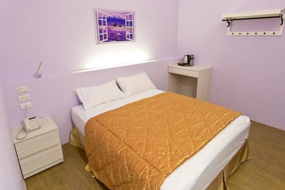 Un dormitorio con cama, mesita de noche con teléfono, mesita auxiliar, estante en la pared y ventana con vista al paisaje.