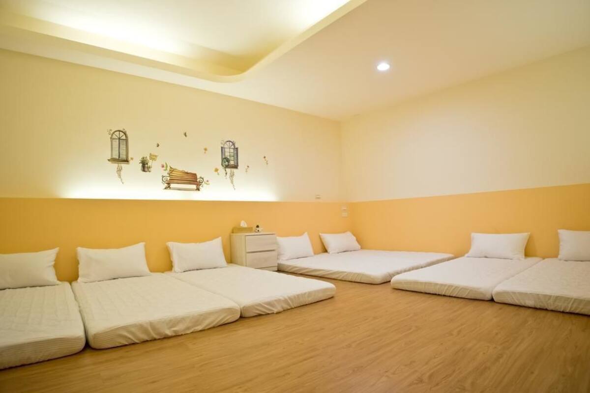 Habitación de hotel con cuatro camas individuales alineadas, una mesita de noche pequeña y decoración en la pared.