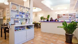 Un área de recepción con mostrador, estanterías con revistas y una planta en maceta.