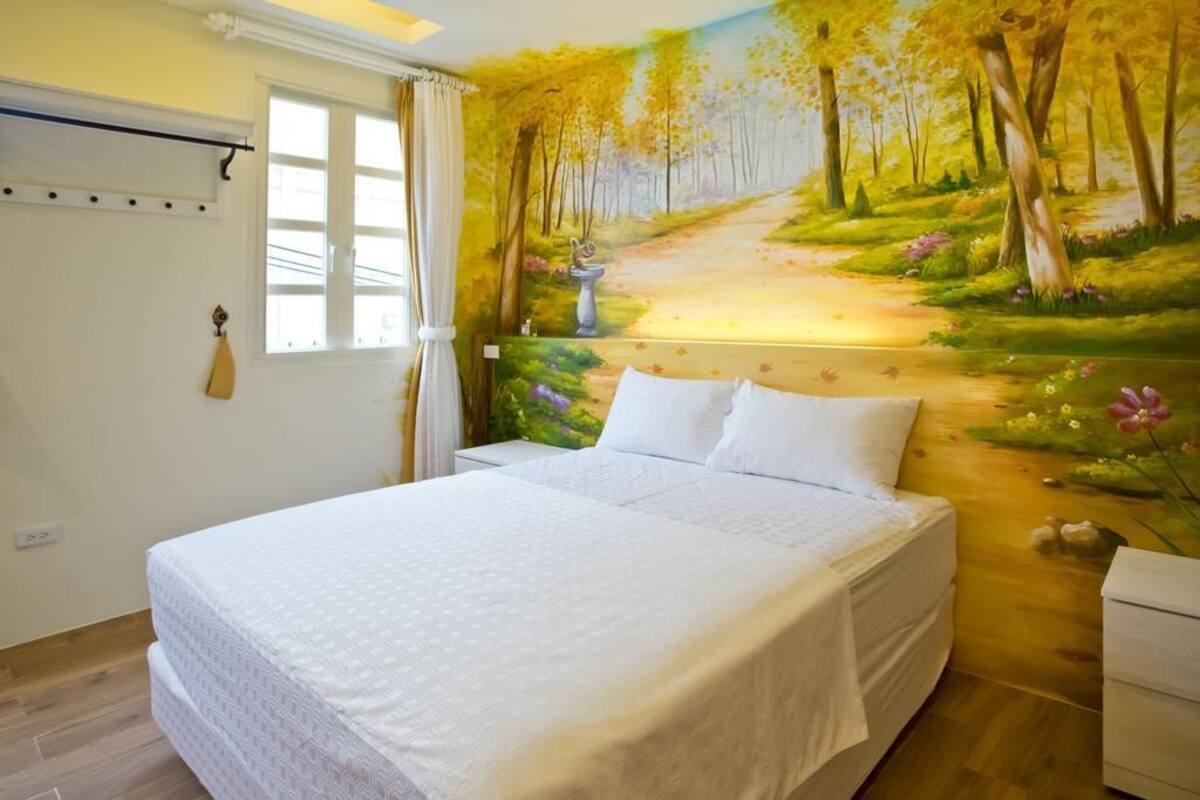 Un dormitorio con una cama grande, una ventana con cortinas y un mural de un sendero en el bosque en la pared.