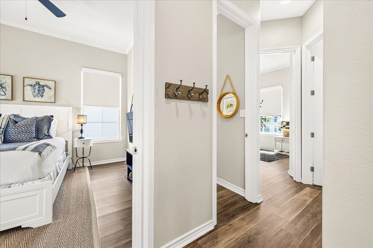 A bedroom with a bed, bedside table, and a window. There is a hallway leading to a bathroom.