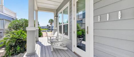 A covered outdoor area with a wooden deck, white chairs, and a view of the ocean.