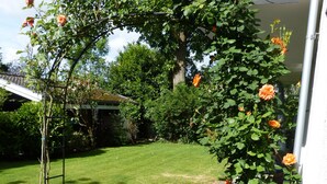 Ein Garten mit einer Rosenbogenpergola, einem gepflasterten Weg und einem Rasen.