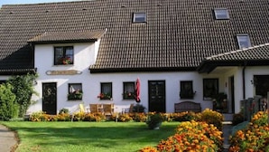 A white building with a tiled roof, a garden with flowers, and outdoor seating.