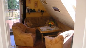 A cozy room with a sofa, a small table with a vase of flowers, and a window overlooking a deck.