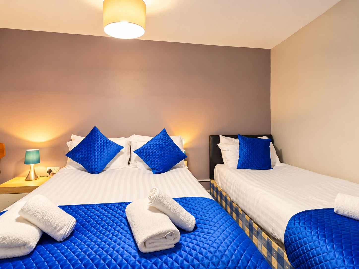 A hotel room with two beds, blue quilted bedspreads, white linens, and a blue and yellow patterned headboard.