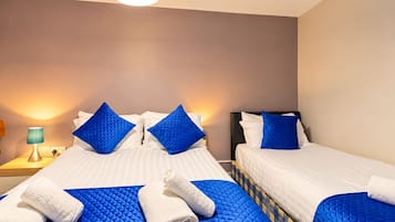 A hotel room with two beds, blue quilted bedspreads, white linens, and a blue and yellow patterned headboard.