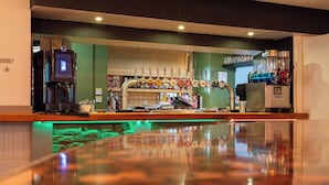 Una zona de bar con una barra larga, una máquina de café, un grifo de cerveza y un dispensador de zumo.